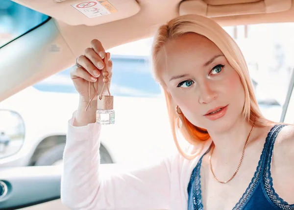Schöne Blondine hängt Auto-Parfüm am Rückspiegel im Auto. — Stockfoto
