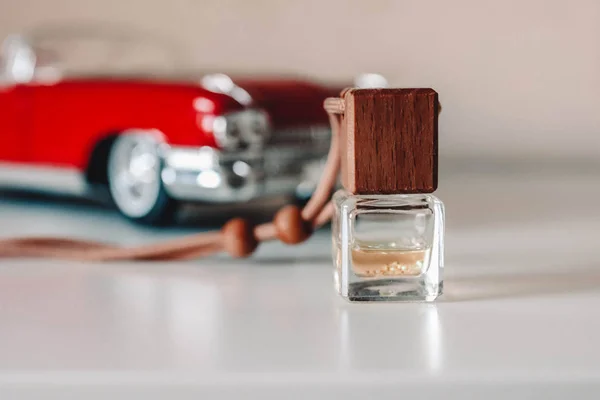 Small glass bottle with aromatic liquid. Car air freshener near toy car model.