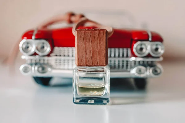 Small glass bottle with aromatic liquid in front of classic car toy model. Concept with car air freshener.