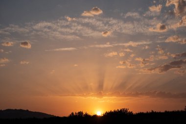 Güneş neredeyse gizlenmiş, bulutlarda gölgeler ve mavi gökyüzü.
