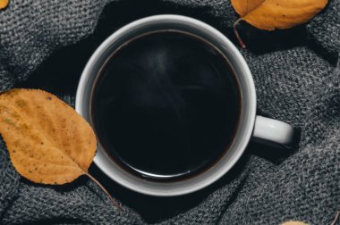 Beyaz kupa, kahve, bir örme eşarp merkezli. Çevresinde sarı yapraklar.