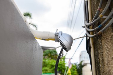 Elektrikli araç, bina girişinin yanındaki prizde koruyucu kapakla şarj ediliyor. Kalın kablo, sürdürülebilir geçiş için güç kaynağına bağlanır