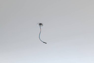 Ev tadilatı sırasında yalnız bir detay. Tek siyah elektrik kablosu beyaz tavandan sarkıyor. İnşaat sürecinin basit bir elementi yeni aydınlatma armatürünü bekliyor.