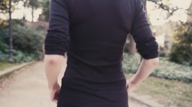 Parkta siyah giyimli genç bir kadın koşudan sonra dinleniyor. Koşmadan önce bacaklarına masaj yapıyor. Kız Park'taki patikada koşuyor. Dışarıdaki hava uygun Loya egzersizleridir