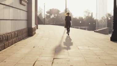 Siyah eşofmanlı genç bir kadın parkta merdivenlerden yukarı koşuyor. Kaçak bir kız. Hava güneşli ve sıcak. Genç bir kız güzel bir şehir parkında spor yaparken merdivenleri koşarak çıkıyor.