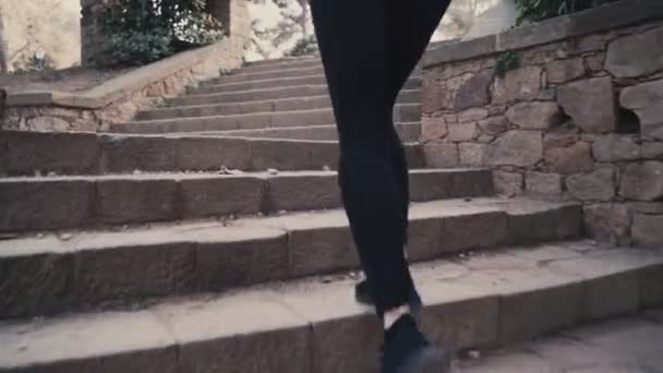 Молода жінка в чорному костюмі біжить по сходах. Дівчинка в бігах. Погода сонячна і тепла. Молода дівчина біжить по сходах під час тренувань у парку — стокове відео