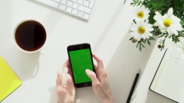 Genç bir kadına klavyede yazarken bir fincan kahve getiriliyor. Kadın, ofis defterleri, klasörler ve telefonundaki bantlarla çevrili sarı bir ofis masasında oturuyor..