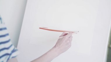 Sanatçı boyayla resim yapıyor. Sanatçı tuval üzerine kırmızı bir suluboya çizer. Beyaz tuval üzerine çizilen kırmızı çizgiler geometrik şekiller oluşturur. Sanatçı ince bir fırça ile çizer