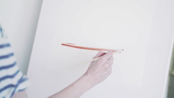 L'artiste peint à la peinture. L'artiste dessine une aquarelle rouge sur toile. Des lignes rouges dessinées sur une toile blanche forment des formes géométriques. L'artiste dessine avec un pinceau fin — Video