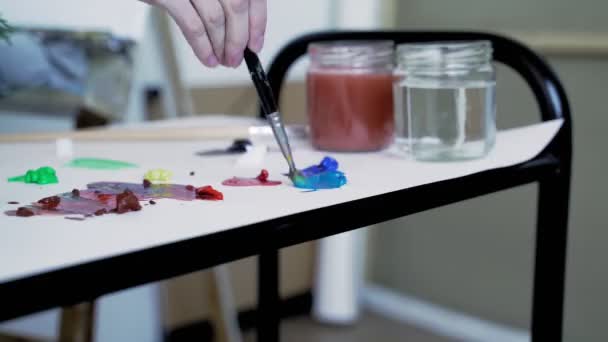 El artista mezcla verde y azul para lograr el color deseado.El artista humedece un pequeño pincel en un recipiente de agua. mezcla diferentes colores . — Vídeos de Stock