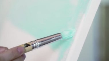 Sanatçı şüskül de duruyor ve açık mavi bir tuval çizer. Adam renkleri karıştırır ve beyaz bir tuvalüzerine koyar. Fırça yoğun hassas boya beyaz tuval leke. Yakın çekim.