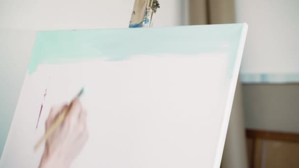 L'artiste se tient au chevalet et dessine la toile bleu clair. Peinture acrylique. L'homme mélange les couleurs et les applique sur une toile blanche comme neige. L'artiste se tient au chevalet . — Video