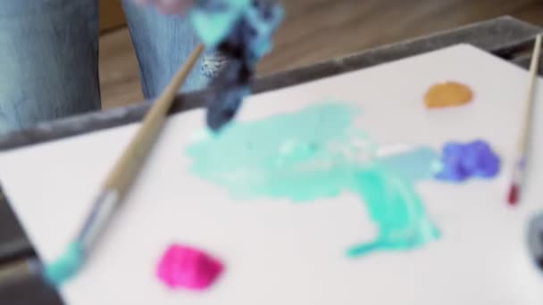 アーティストは、パレットにペイントを追加します。芸術的なパレットに滴る塊をペイントします。アーティストは繊細な春のフラワーパレットを形成します。穏やかな青いアクリル塗料は、パレット上のチューブから絞り出されます — ストック動画