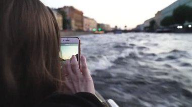 Genç ve güzel bir kız tekne gezisi sırasında telefonla fotoğraf çekiyor. Saint Petersburg, Leningradskaya Oblastı / Rusya - 22.08.2019: Saint Petersburg, Rusya 'nın nehir ve kanallarına tekne gezisi. Küçük dalgalar, parklar, saraylar.