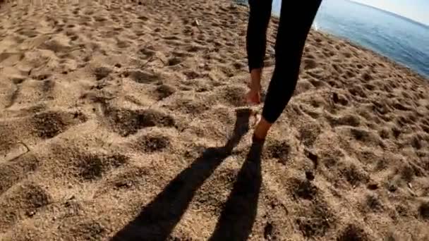 A fekete neoprén öltönyös lány a homokos tengerparton megy a tengerhez. Napos nap a faluban. Triatlon. Úszásra kész. Úszás nyílt vízben. Reggeli úszás. Tengerparti mediterrán város — Stock videók