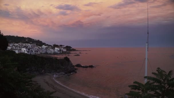 小さな海岸沿いの地中海の町で美しい夕日。バイオレットとピンクの空と紫の海。海岸沿いの白い家。平和と静か。夕焼け空にピンクの雲。海での休日 — ストック動画