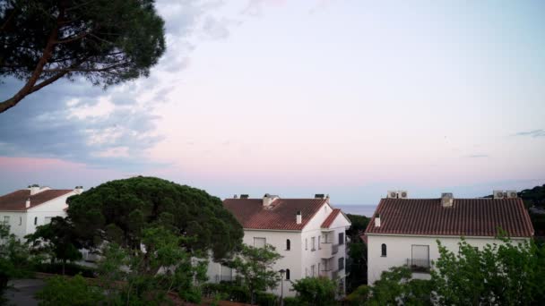 Прекрасний захід сонця в невеликому прибережному середземноморському місті. Фіолетове і рожеве небо і фіолетове море. Білі будинки на узбережжі. Мир і тиша. Рожеві хмари на заході сонця. Відпочинок на морі — стокове відео