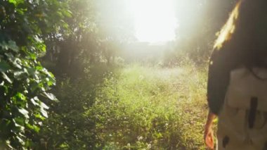 Yürüyüş. Sırt çantalı bir kız orman yolunda yürüyor ve güzel bir günbatımının tadını çıkarıyor. Yeşil ormandaki altın ışık. Orman yürüyüşü. Güneşli bir yaz günü. Ağaçların ve çiçeklerin arasında yürüyorum. Tatiller.