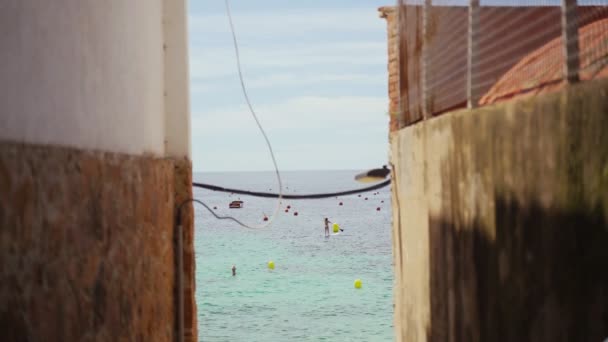 Gyönyörű kilátás nyílik a tengerre egy keskeny utcáról egy kis mediterrán városban. A falu a lenyűgöző smaragd öböl partján van. Napsütéses nyári nap a tenger mellett. Nyaralás a parton. Festői utca.. — Stock videók