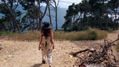 Yürüyüş. Sırt çantalı bir kız mavi deniz boyunca bir orman yolunda yürüyor. Ormanda yürüyüş. Yeşil ormandaki altın ışık. Orman yürüyüşü. Güneşli bir yaz günü. Ağaçların arasında yürüyorum. Tatiller. 