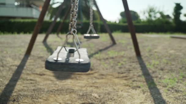 A wooden swing sways on the park playground. Swing in the green garden. Summer games in the garden. Summer holidays. Hot sunny day. — Stock Video