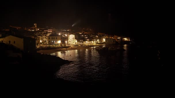 Vista de uma bela aldeia costeira à noite. Pequena cidade mediterrânica. Casas brancas numa praia de areia. Férias na costa. Luz nas janelas é refletida nas ondulações do mar . — Vídeo de Stock