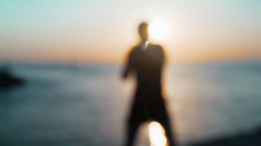 Sabah sporu. Deniz rıhtımında Muay Thai Kutusu eğitimi. Denizin arka planına ve yükselen güneşe karşı tekme pratiği yapan genç adam. Spor aktivitesi. Sporcu. Yumruk, dirsek. Yumruk antrenmanına yakın çekim