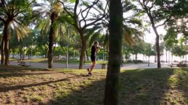 Sabah sporu. Parkta Muay Thai Kutusu eğitimi. Genç adam güneşli şehir parkında koşuyor ve yumruk ve tekme pratiği yapıyor. Spor aktivitesi. Sporcu. Zıplıyor ve koşuyor. Yumruk, dirsek, diz.