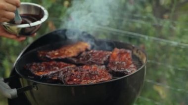 Arkadaşlarla yaz barbeküsü. Izgara domuz pirzolası. Şefin elleri domuz kaburgalarını ev yapımı barbekü sosuyla fırçalarken. Lezzetli yemekler. Açık hava yemeği. Izgara et ızgarada tütüyor..