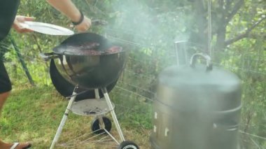 Arkadaşlarla yaz barbeküsü. Ev yapımı barbekü soslu ızgara domuz pirzolası. Aşçı domuz pirzolası ve maşayı tabağa koyar. Lezzetli yemekler. Açık hava yemeği. Izgara et ızgarada tütüyor..