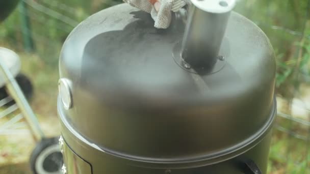 Barbacoa de verano con amigos. Costillas de cerdo a la parrilla con salsa.. Primer plano de las manos del cocinero abriendo la tapa del ahumadero. Comida sabrosa. Comida al aire libre. La carne a la parrilla está fumando en la red de parrilla. — Vídeo de stock