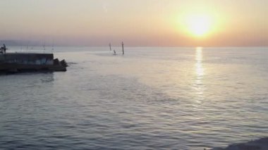 Güneş iskelede doğuyor. Sakin bir sabah denizi. İskelede olta kamışı. Renkli gökyüzünde parlak güneş. Deniz kenarında sakin bir sabah.