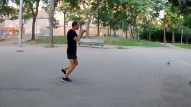 Sabah sporu. Parkta Muay Thai Kutusu eğitimi. Genç adam güneşli şehir parkında koşuyor ve yumruk ve tekme pratiği yapıyor. Spor aktivitesi. Sporcu. Zıplıyor ve koşuyor. Yumruk, dirsek, diz.