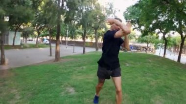 Sabah sporu. Parkta Muay Thai Kutusu eğitimi. Genç adam güneşli şehir parkında koşuyor ve yumruk ve tekme pratiği yapıyor. Spor aktivitesi. Sporcu. Zıplıyor ve koşuyor. Yumruk, dirsek, diz.