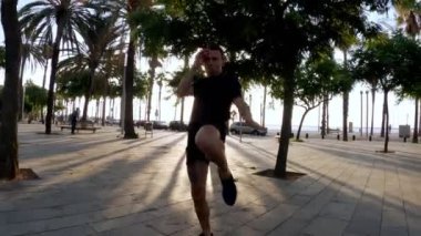 Sabah sporu. Parkta Muay Thai Kutusu eğitimi. Genç adam güneşli şehir parkında koşuyor ve yumruk ve tekme pratiği yapıyor. Spor aktivitesi. Sporcu. Zıplıyor ve koşuyor. Yumruk, dirsek, diz.