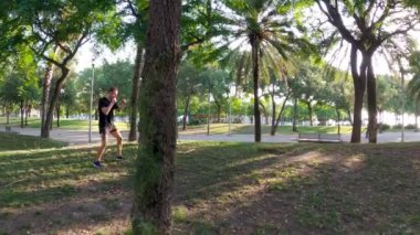 Sabah sporu. Parkta Muay Thai Kutusu eğitimi. Genç adam güneşli şehir parkında koşuyor ve yumruk ve tekme pratiği yapıyor. Spor aktivitesi. Sporcu. Zıplıyor ve koşuyor. Yumruk, dirsek, diz.