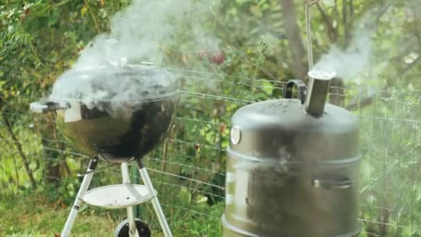 Bahçede arkadaşlarıyla barbekü yapıyor. Dumanı tüten bir barbekü ve ev yapımı bir tütsüleme evinin yakın çekimi. Barbekü için daha hafif kömür. Portatif barbeküde buharlı kömür. Lezzetli ev yemekleri.. — Stok video