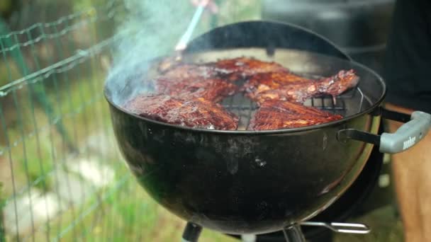 Barbacoa de verano con amigos. Costillas de cerdo asadas. Primer plano de un chefs manos cepillado costillas de cerdo con salsa barbacoa casera. Comida sabrosa. Comida al aire libre. La carne a la parrilla está fumando en la red de parrilla. — Vídeos de Stock