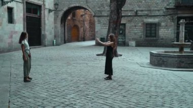 Taş duvarın önünde fotoğraf çektirmek için poz veren uzun saçlı güzel bir esmer. Genç ve çekici bir kadın güzel bir meydanda arkadaşının fotoğraflarını çekiyor. Turist cep telefonuyla portre yapıyor.
