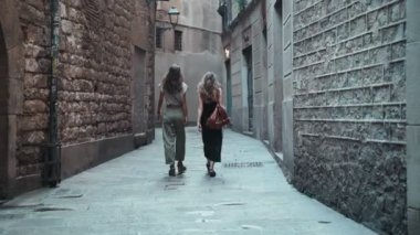 İki arkadaş güzel şehirde dolaşıyorlar. Ortaçağ kasabasının taştan sokaklarında yürüyen iki uzun saçlı genç kadın. İki turist etrafı geziyor. Siyah elbiseli kız. Pantolon giyen kız..