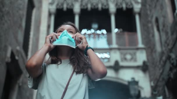 Beautiful long-haired brunette puts on protective mask. Young attractive woman is protecting herself from infection. COVID-19 precaution. Stay safe. Coronavirus. Pretty tourist girl in a grey t-shirt. — Stock Video