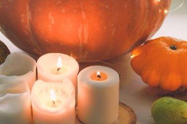 Yanan beyaz mumlar ve turuncu balkabakları.