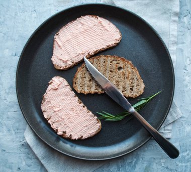 Dilimlenmiş çavdar ekmeği, ezmeli ve biberiyeli siyah tabakta.