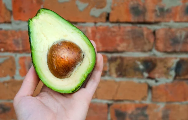 Weibliche Hand Hält Halbierte Avocado Mit Kern Auf Backsteinwand Hintergrund — Stockfoto