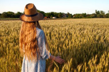 Buğday tarlasında uzun sarı saçlı ve hasır şapkalı bir kadın..