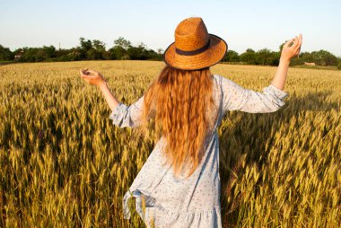 Buğday tarlasında uzun sarı saçlı ve hasır şapkalı bir kadın..