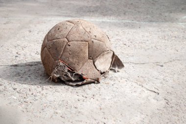 Eski, sönük, hırpalanmış bir futbol topu ve büyük bir delik. Kaldırımda, metin için yer