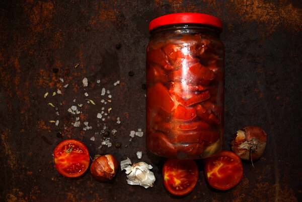 Банка с сушеными помидорами, морской солью, луком и чесноком на ржавом фоне.