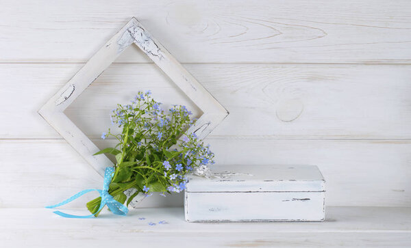 Forget-me-not flowers bouquet, vintage casket and photo frame on white wooden shabby board in provence style