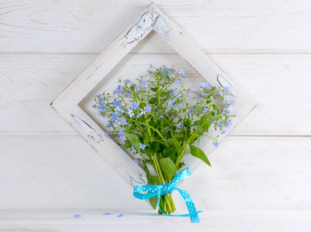 Forget-me-not flowers bouquet and vintage photo frame on white wooden shabby board in provence style